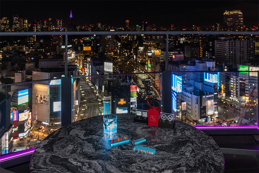 CÉ LA VI TOKYOから見える夜景とテーブルの上に置かれたすべてのIQOS イルマ WE 2023 限定モデル、カクテル